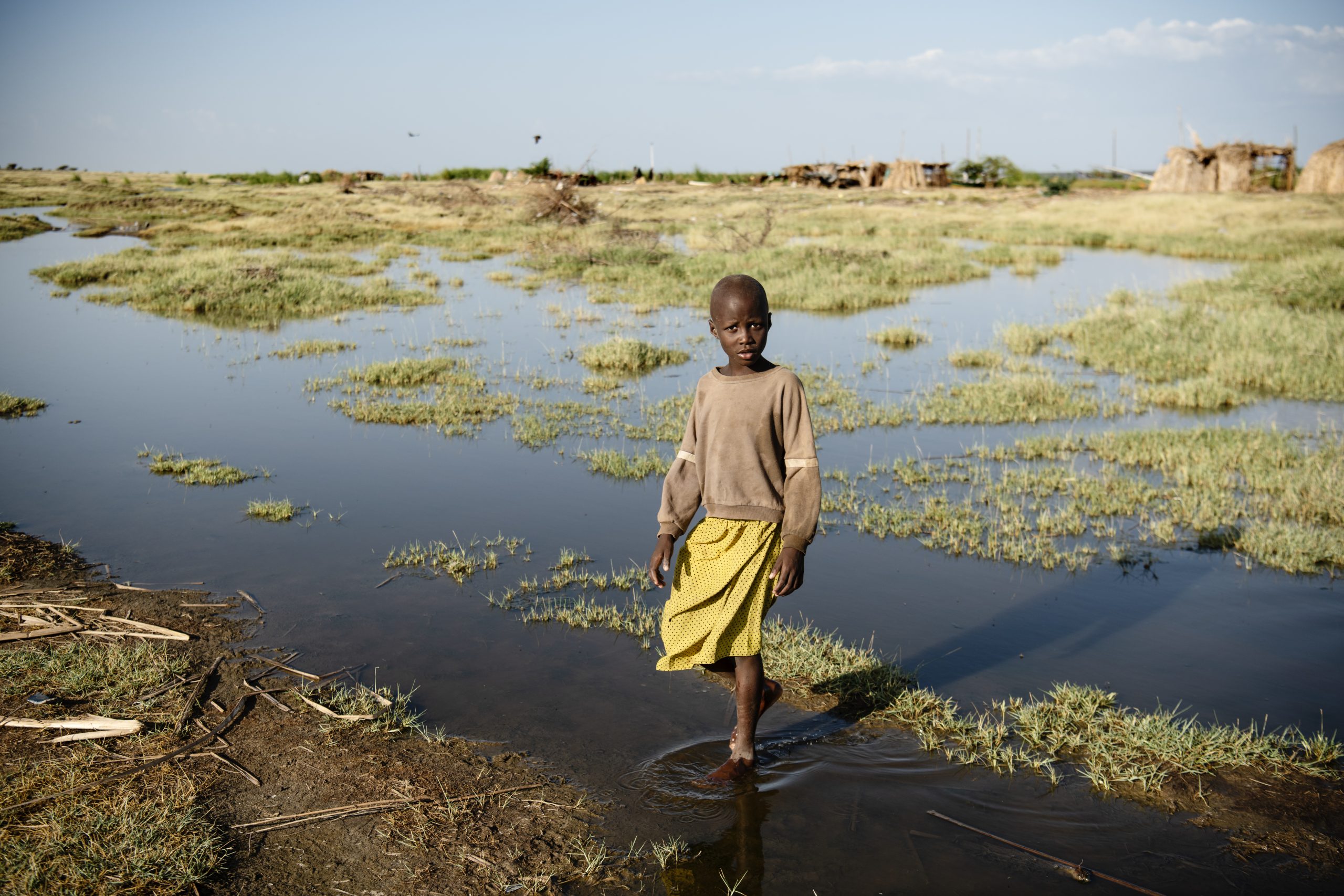 Aminit, pige fra Kenya i gul kjole st&aring;r i vand. Illustration for klimaforandringer.