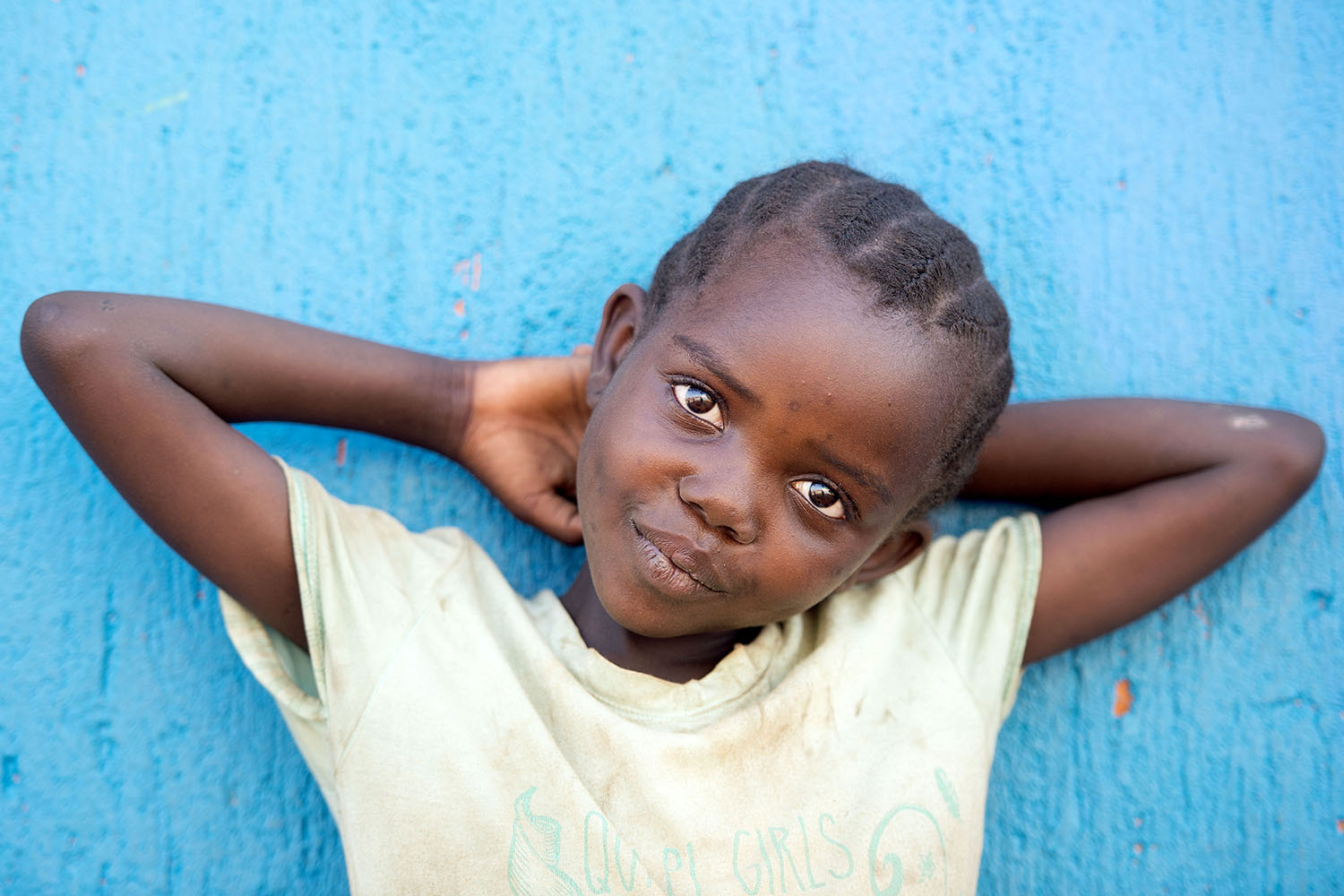 Ung pige poserer med h&aelig;nderne bag hovedet op ad bl&aring; mur. Illustration: Folkekirkens N&oslash;dhj&aelig;lp.