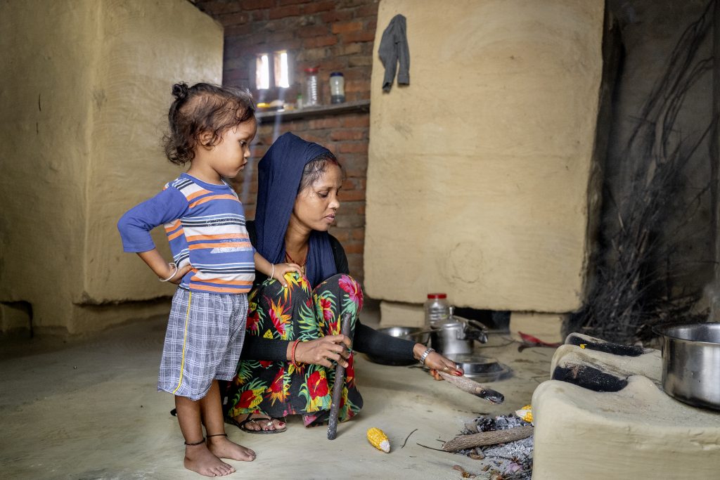 En pige og en kvinde siddende på hug og starter bål til madlavning