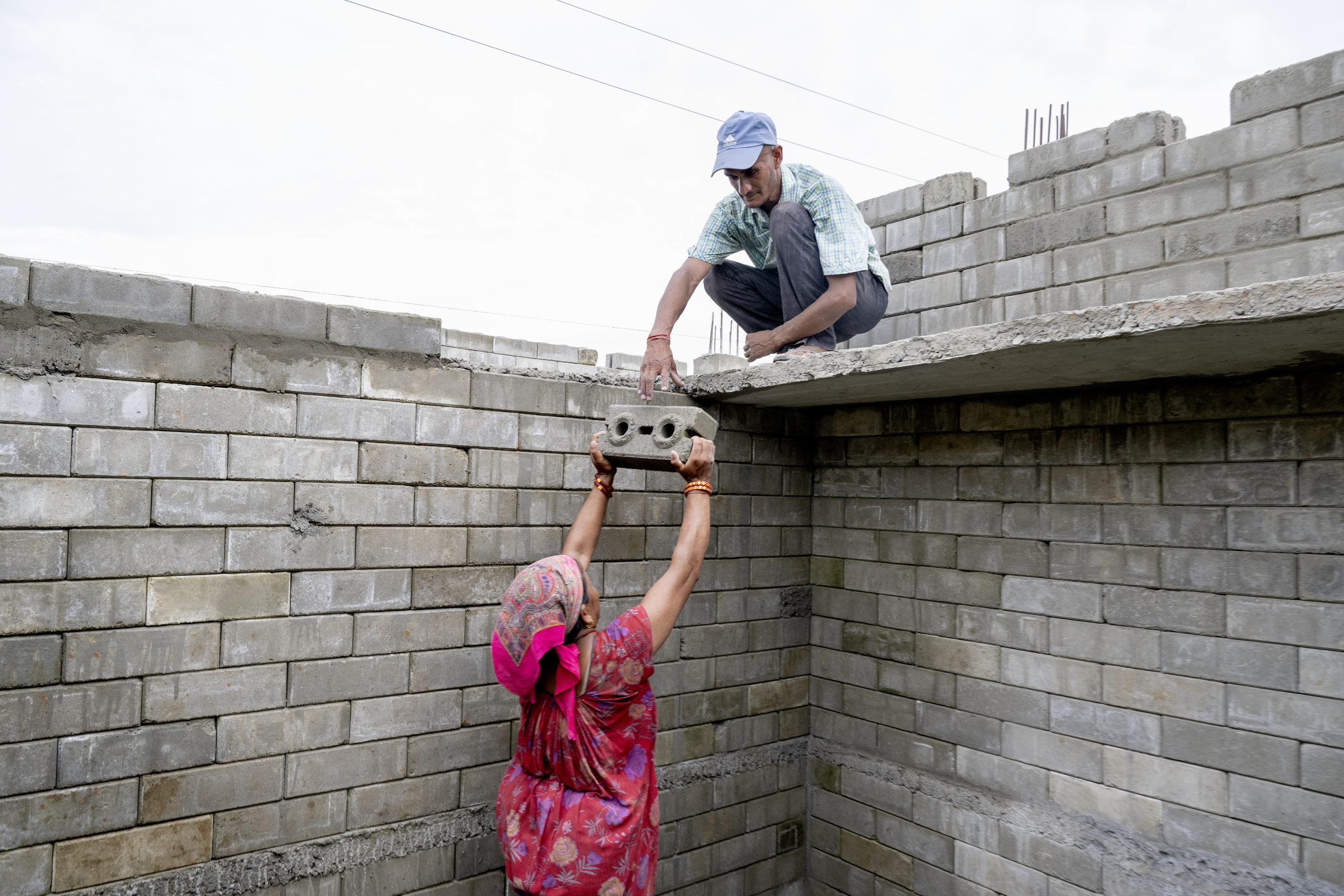 Kvinde iført rød kjole løfter en mursten til en mand