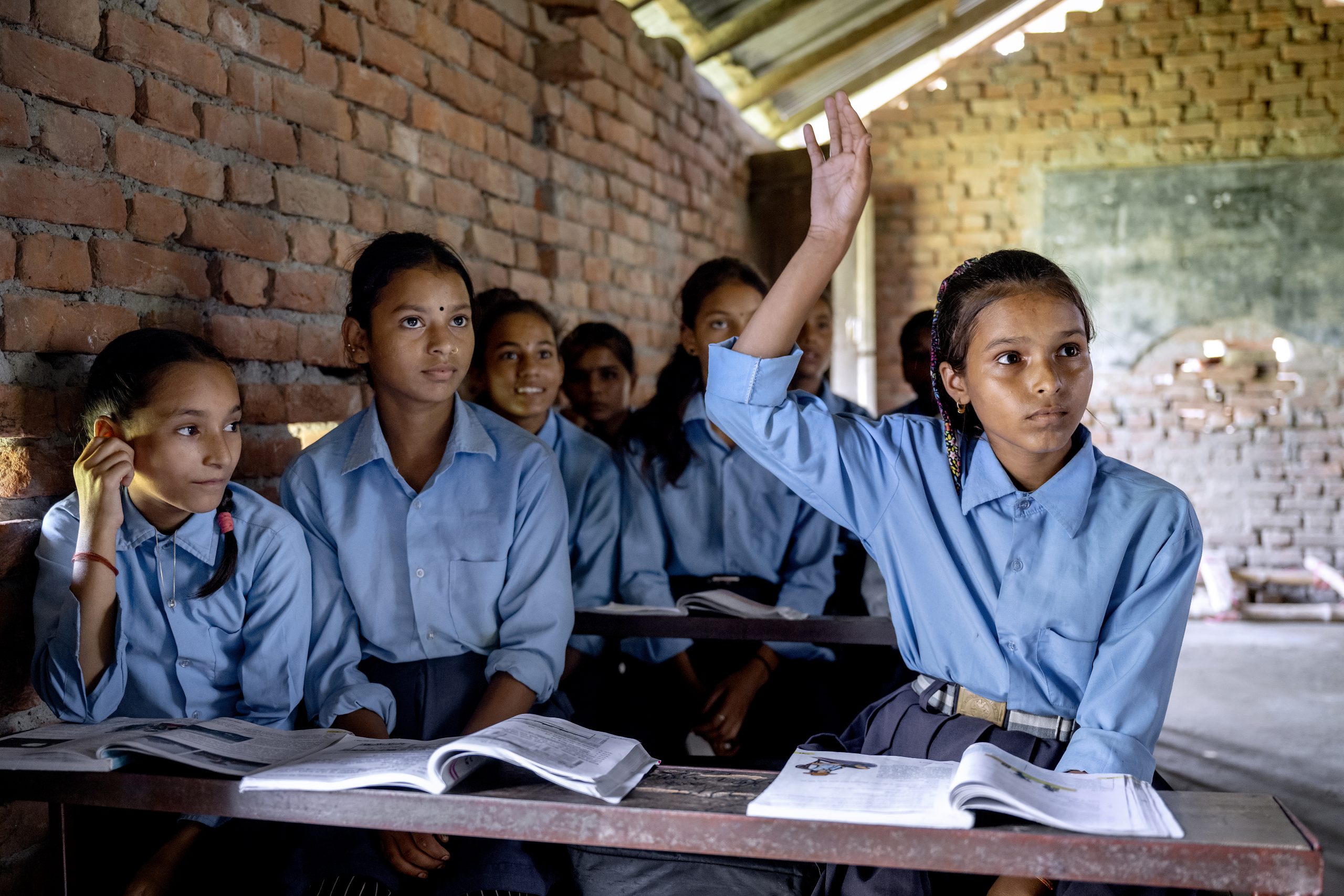 Elever if&oslash;rt bl&aring; skjorter sidder p&aelig;nt p&aring; skoleb&aelig;nken og r&aelig;kker h&aring;nden op